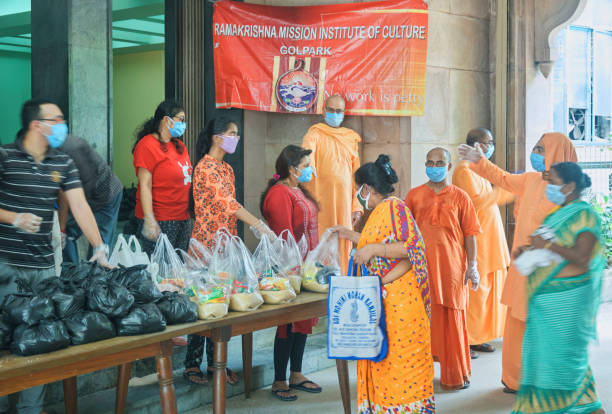 Group of volunteers and monks of Ramakrishna Mission (Golpark) wearing traditional saffron dresses, donating everyday essential foods to poor & needy people. Plastic pouch of raw foods are visible on desk. 

Photo taken at Ramakrishna Mission Institute of Culture, Golpark, Kolkata on 05/05/2020. During coronavirus lockdownin city.